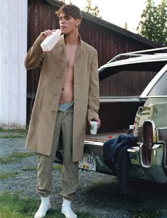 a man standing in front of a car drinking from a cup