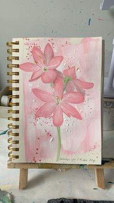 a painting with pink flowers on it sitting on top of a wooden easel next to paintbrushes