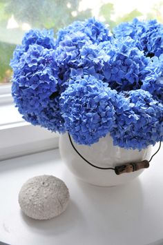 a white vase filled with blue flowers on top of a window sill next to a rock