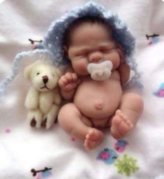 a baby laying next to a teddy bear on a blanket with a blue bonnet and pacifier