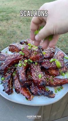 someone is picking up some meat on a plate with sesame seeds and green onion sprinkles