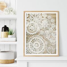 a white fireplace mantle with a framed lace doily art piece on it