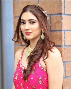 a woman in a pink dress standing next to a brick wall and smiling at the camera