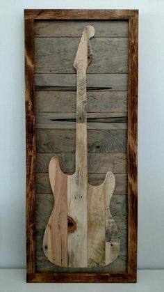 a wooden guitar hanging on the wall in front of a white wall with wood planks