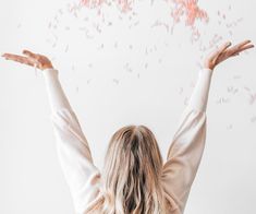 a woman with her arms outstretched in front of a white wall that has pink speckles on it