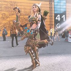 a woman dressed up as a warrior holding a bow and arrow in front of a building