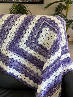 a purple and white crocheted blanket sitting on top of a black leather couch