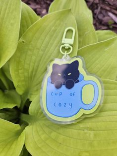 a cup of cozy keychain sitting on top of a green leafy plant