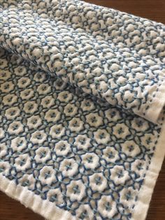 two pieces of blue and white crocheted fabric on a wooden table with wood flooring