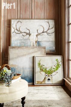 a living room with deer head paintings on the wall and an ottoman in front of it