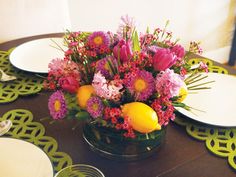 a vase filled with flowers and lemons on top of a wooden table next to plates