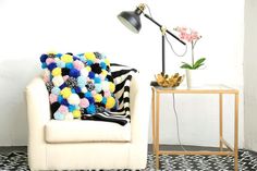 a white chair with a black and yellow blanket on it next to a table with a potted plant