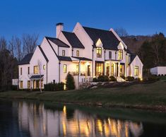 a large white house sitting on top of a lush green hillside next to a lake