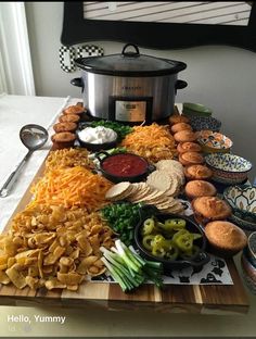 a wooden cutting board topped with food next to a crock pot filled with cheese