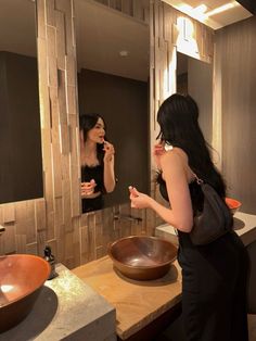 a woman standing in front of a bathroom mirror brushing her teeth and looking at herself in the mirror