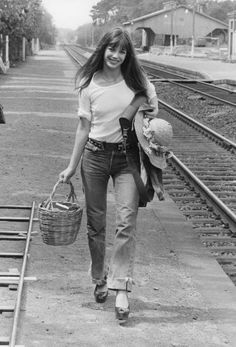 a woman walking down the train tracks carrying a basket