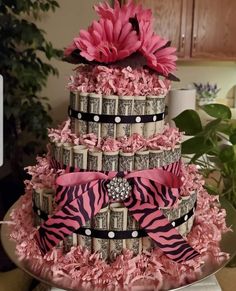 a three tiered cake with pink flowers and money wrapped around the bottom, sitting on a silver platter