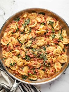 a skillet filled with pasta and spinach on top of a marble countertop