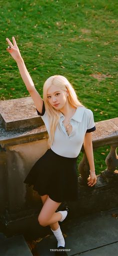 a young woman posing for a photo in front of a stone bench with her hand up