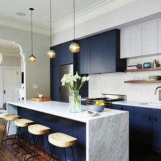 a kitchen with blue cabinets and marble counter tops, stools at the center island