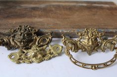 three antique brass drawer pulls on a white surface with an old wooden box in the background