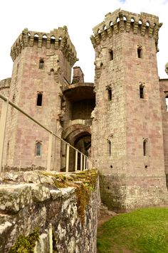 an old castle with two towers on the top and one at the bottom that is surrounded by grass