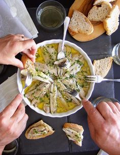 two people eating soup from a bowl with bread on the side and wine glasses next to them