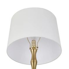 a lamp with a white shade on top of it and a gold metal base underneath