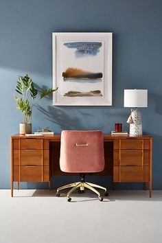 a desk with a pink chair in front of it and a painting on the wall