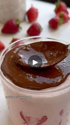 a spoon in a cup with chocolate sauce on it and strawberries around the bowl