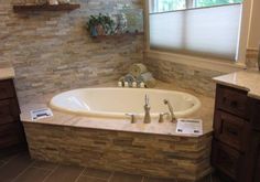 a bathroom with a stone wall and large bathtub in the corner, along with wooden cabinets