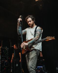 a man with tattoos on his arm playing guitar and singing into a microphone at a concert