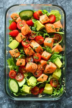 a salad with salmon, avocado and tomatoes in a glass dish on a table