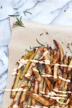 some french fries with sauce on top of them sitting on a piece of parchment paper