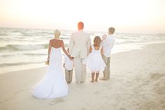 a bride and groom walking with their children on the beach