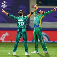 two men in green and yellow uniforms are standing on the field with their arms outstretched