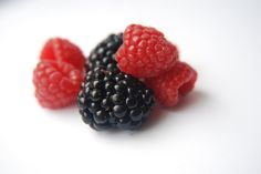 raspberries and blackberries on a white surface with one berry still in the foreground