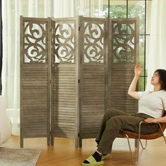 a woman sitting on a chair in front of a room divider