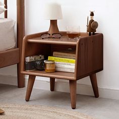 a wooden shelf with books, glasses and a camera on it next to a bed