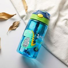 a blue and green water bottle sitting on top of a white table next to leaves