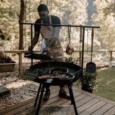 a man grilling food on top of an outdoor bbq with chains hanging from it