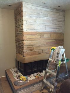 a man standing on a step ladder in front of a brick fireplace that is being built