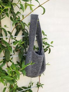 a handbag hanging on a wire fence next to some green plants and leaves in front of a white wall