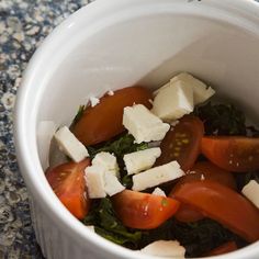 a white bowl filled with tomatoes, cheese and spinach