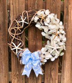 a wreath with starfish and seashells hanging on a wooden fence next to a blue bow