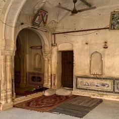 an old room with rugs and paintings on the walls, ceiling fan and doorway