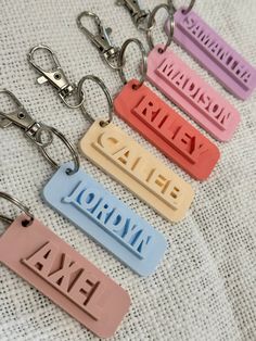 four key chains with different colored name tags attached to them on a white fabric background