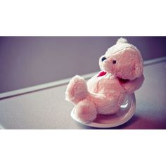 a small pink teddy bear sitting on top of a white saucer with one paw in the air