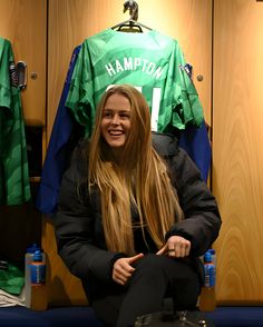 a young woman sitting in front of lockers holding a green jersey and smiling at the camera