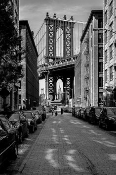 a black and white photo of cars parked on the street in front of a bridge